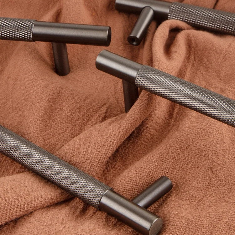 "Solid brass knurled cabinet handle with gunmetal finish and textured bar detail on terracotta fabric background"