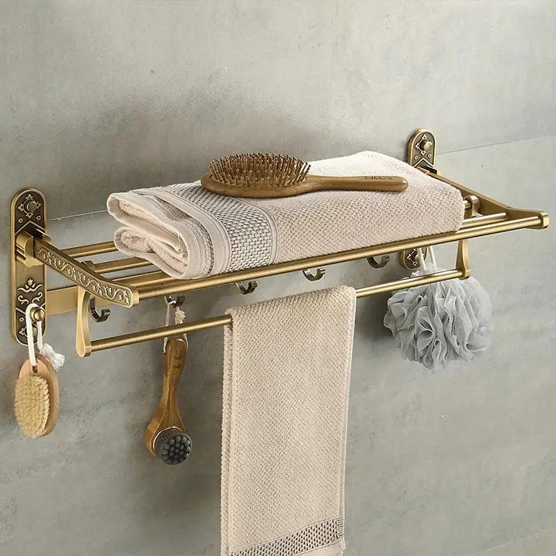 Gold towel rack with towels and bathroom accessories on a gray wall.