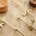 Four gold-finished bamboo branch cabinet handles arranged diagonally on a light wood tabletop, with decorative woven baskets and wooden objects in the background.